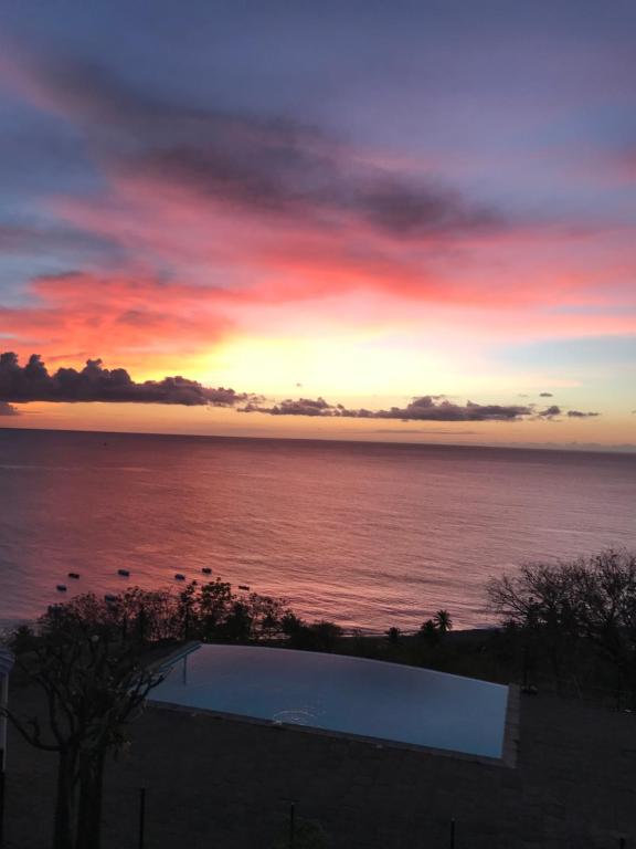 una puesta de sol sobre un cuerpo de agua con una piscina en Morne Charlotte en Le Carbet