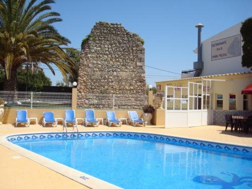 uma piscina com cadeiras azuis e um edifício em Torre Velha AL em Albufeira