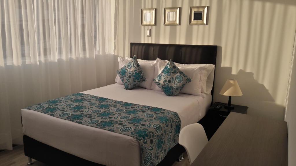 Hotel Rosales Plaza في مانيزاليس: غرفة نوم مع سرير ووسائد زرقاء وبيضاء