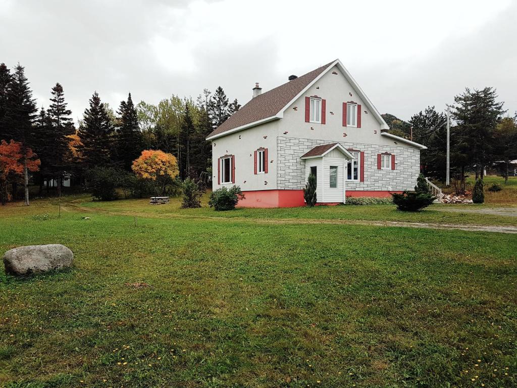 una casa blanca con adornos rojos en un campo en Chill Shack - Auberge Jeunesse, en Sainte-Anne-des-Monts