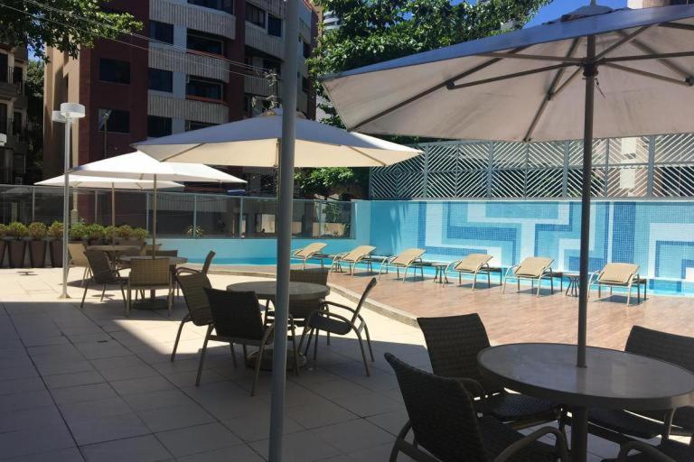 un grupo de mesas y sillas con sombrillas junto a una piscina en Apartamento Ondina Choice, en Salvador