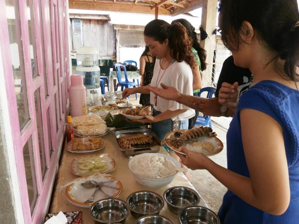 a group of people standing around a table with food at Hogarista Homestay in Kaledupa