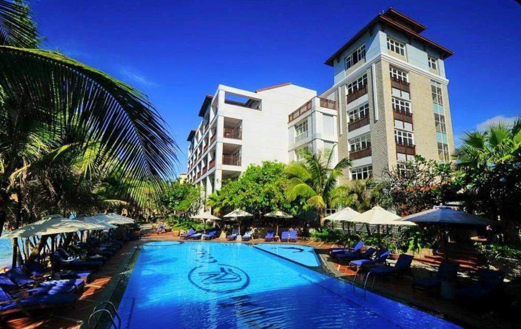 a hotel with a swimming pool with chairs and a building at Novela Muine Resort & Spa in Mui Ne