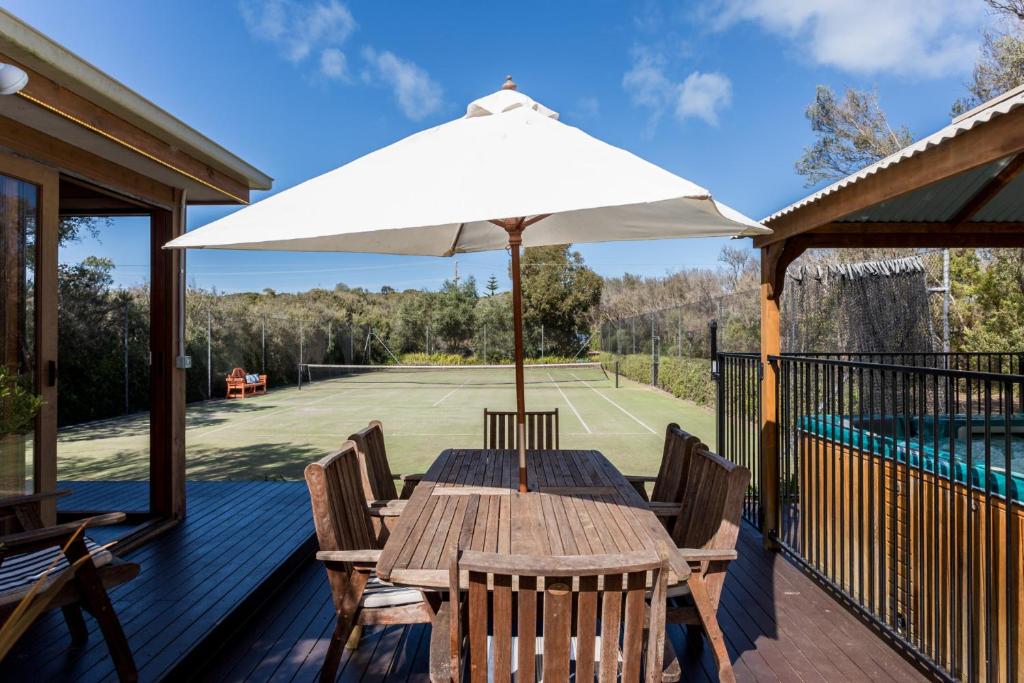 a wooden table with an umbrella on a tennis court at The Heyfield Hideaway: Tennis & Spa in Rye