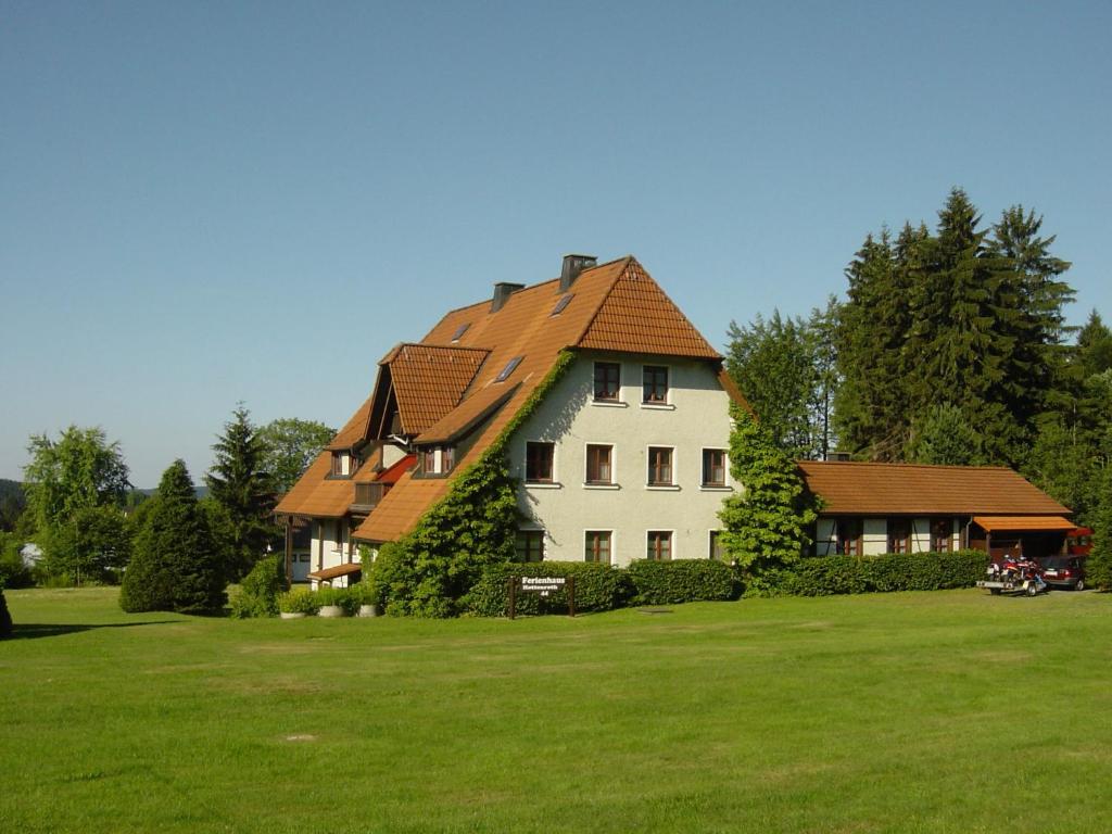 a large house with a roof on a green field at ferienwohnungen hottenroth in Warmensteinach