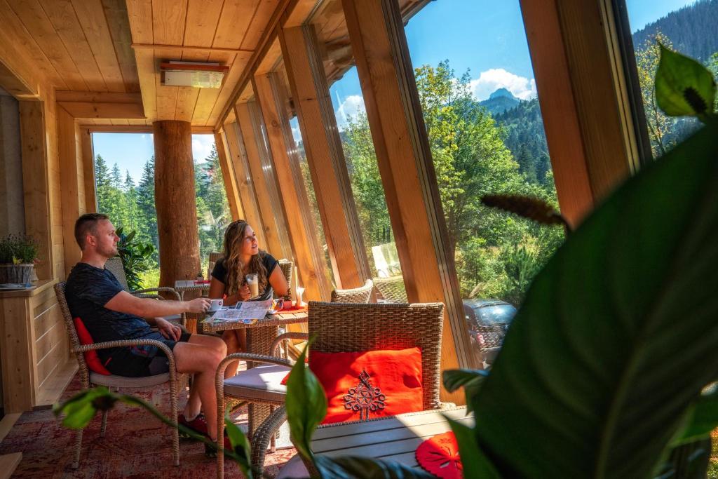 a man and a woman sitting at a table in a room with windows at Hotel Eco Tatry Holiday& Spa in Kościelisko