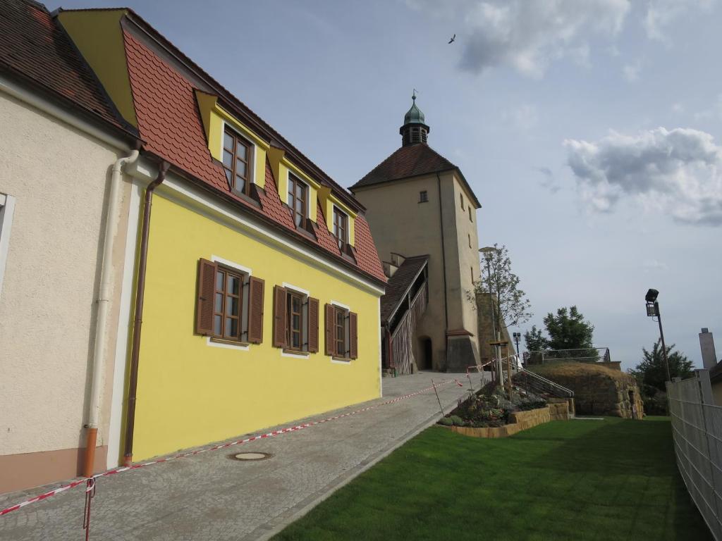 ein gelbes Gebäude mit einem Turm und einem grünen Hof in der Unterkunft Ferienwohnung am Blasturm in Schwandorf in Bayern