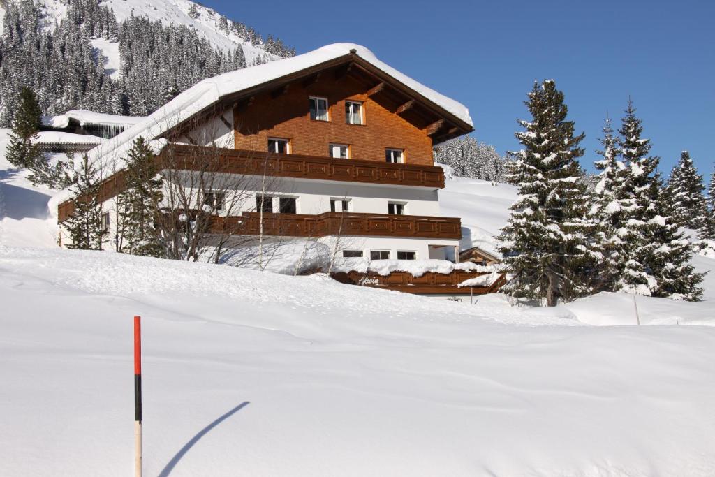 duży drewniany budynek w śniegu z drzewami w obiekcie Pension Alwin w Lech am Arlberg