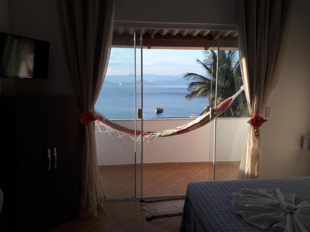 a bedroom with a large window with a view of the ocean at Suítes Encanto do Pai in Praia de Araçatiba