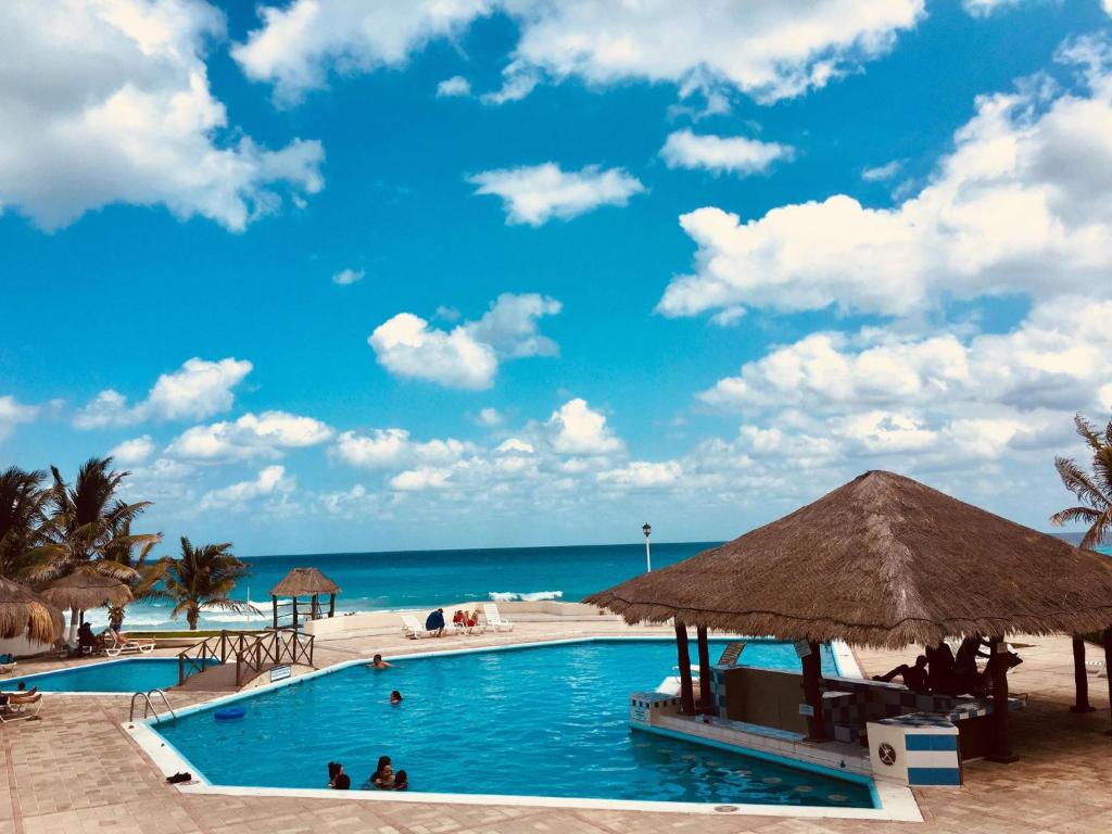 a pool at the beach with a blue sky and the ocean at Brisas Apartment ZH in Cancún
