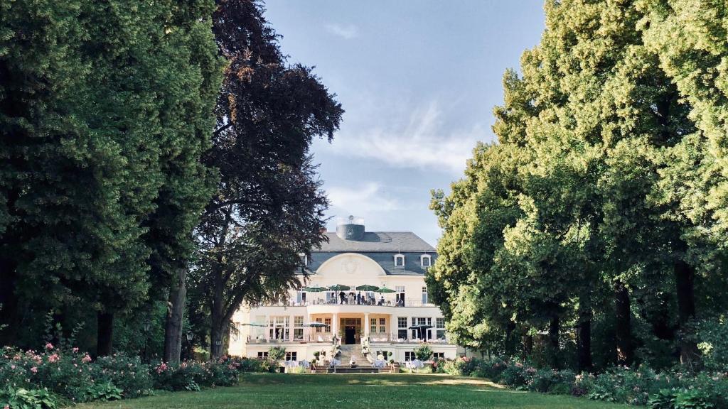 una grande casa bianca con alberi di fronte di Hotel Schloss Teutschenthal a Teutschenthal