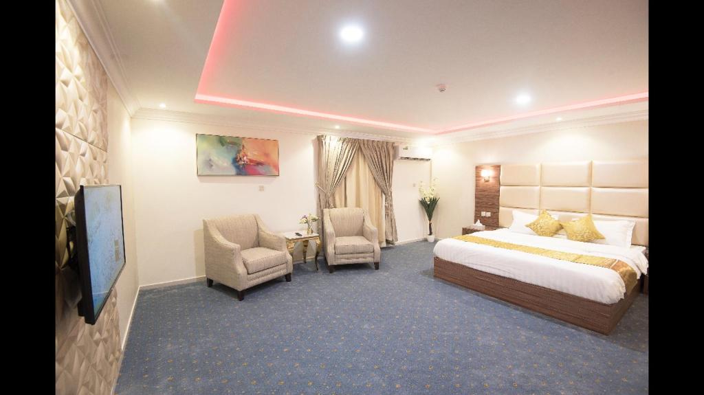 a hotel room with a bed and a tv and chairs at Janan Al Nakheel Serviced Apartments in Al Muzāḩimīyah
