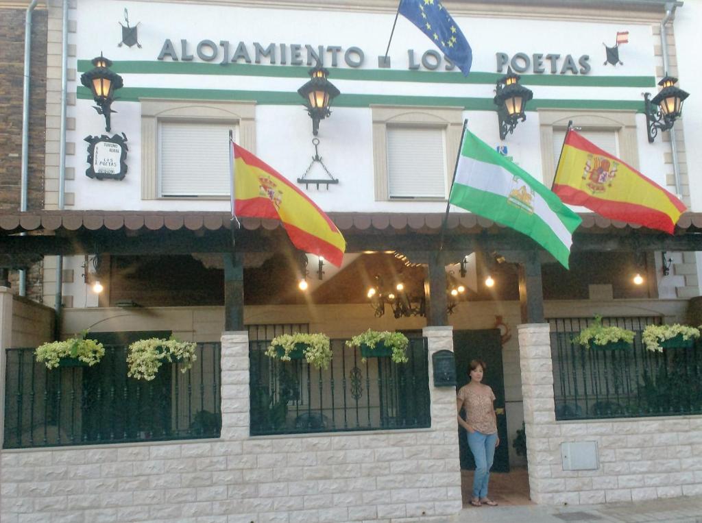 un hombre parado frente a un edificio con banderas en Alojamiento Los Poetas, en Baeza