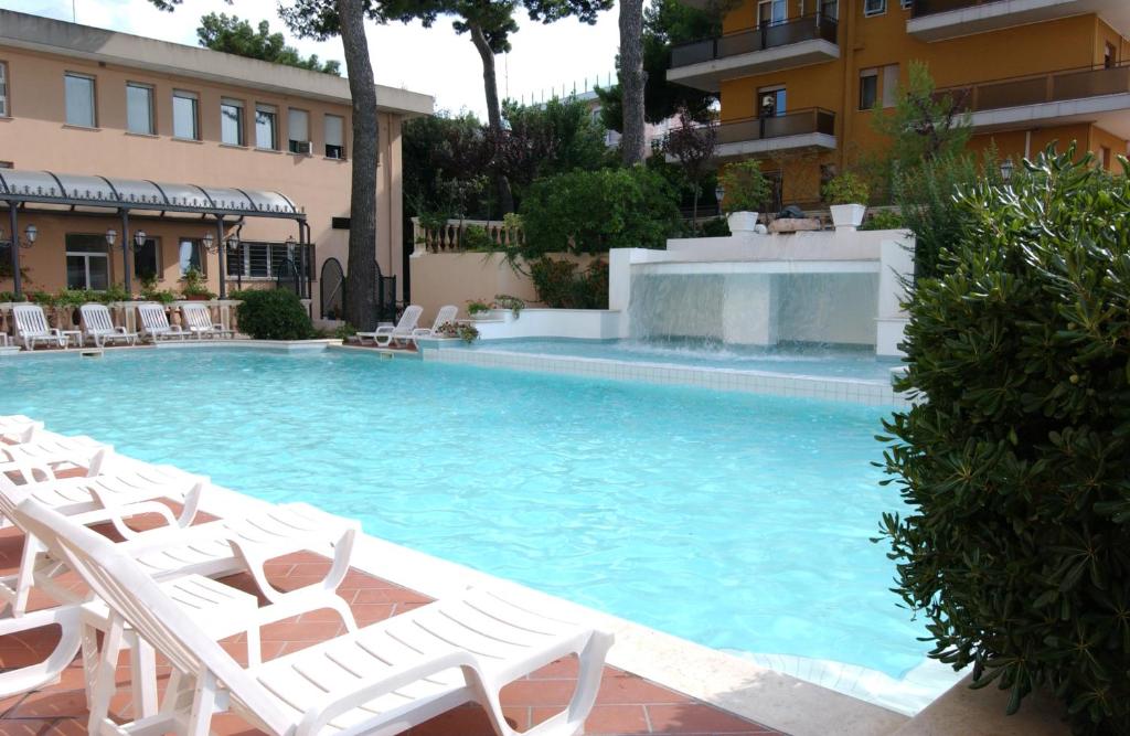 una piscina con sedie a sdraio bianche e una piscina di Hotel Milano Helvetia a Riccione