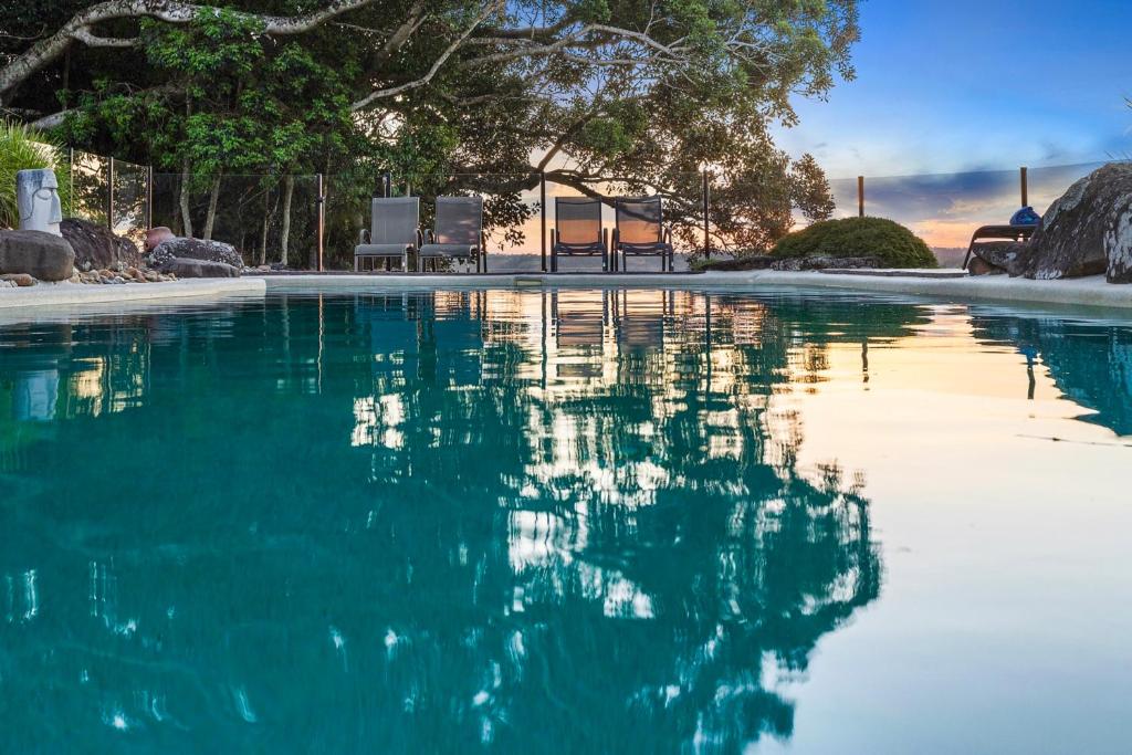 una piscina de agua azul con sillas y árboles en Byron Hinterland Villas, en Clunes