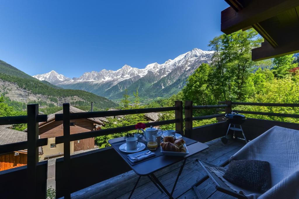 a table with a plate of food on a balcony with mountains at Chalet Noemie in Les Houches