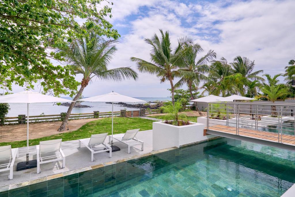 a pool with chairs and umbrellas next to the ocean at Les Estivales Beachfront Suites & Penthouses by LOV in Trou aux Biches