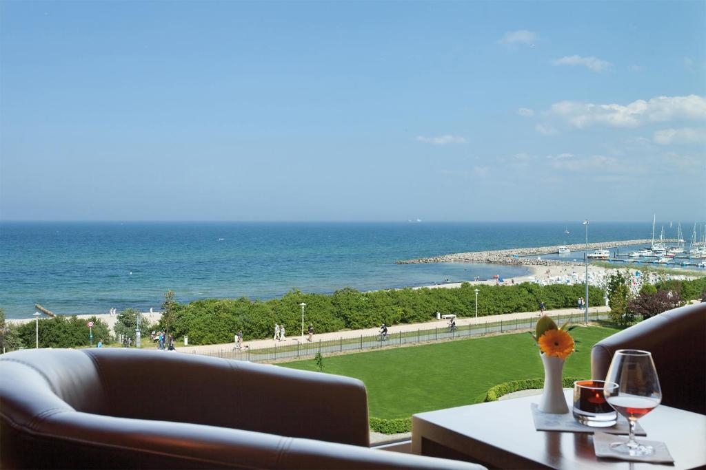 a table with a glass of wine and a view of the ocean at Morada Strandhotel Ostseebad Kühlungsborn in Kühlungsborn