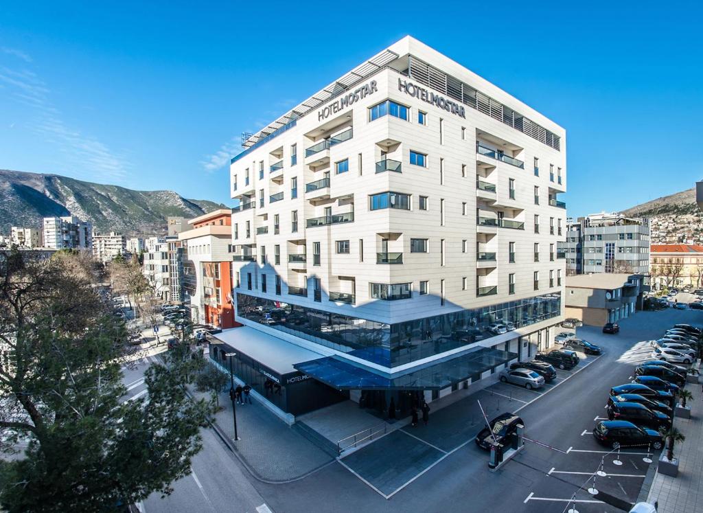 a tall white building with a parking lot in a city at Hotel Mostar in Mostar