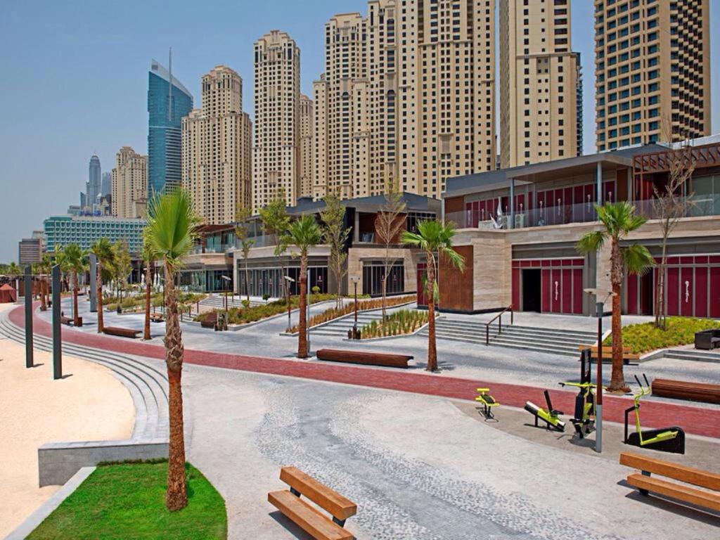 a park with benches and palm trees in a city at Murjan Suites Waterfront The Walk Jumeirah Beach Residence in Dubai