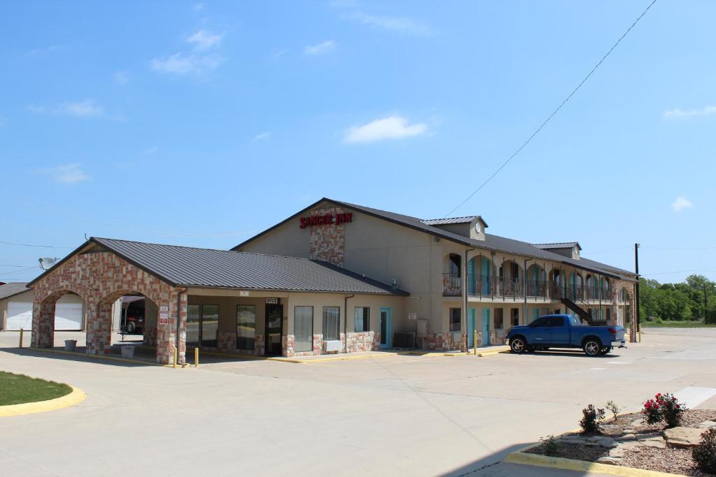 a building with a blue truck parked in a parking lot at Sanger Inn in Sanger