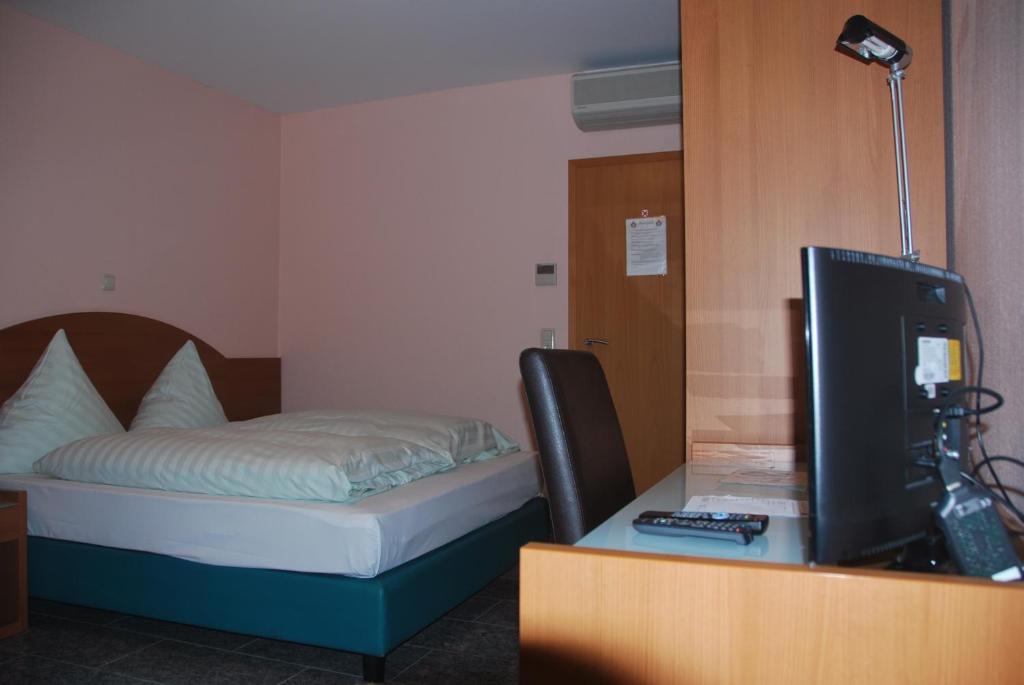 a room with a bed and a desk with a television at Hotel & Restaurant Garda in Darmstadt