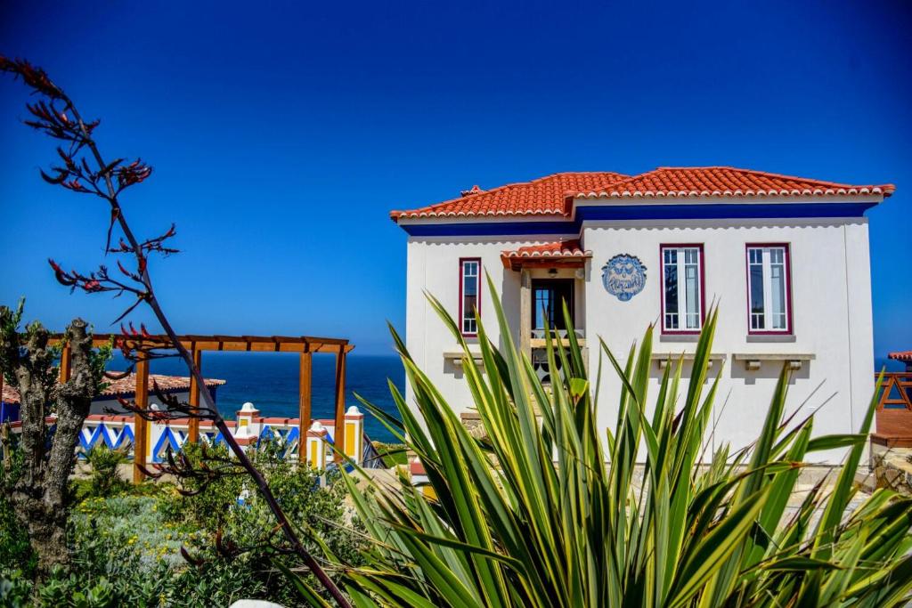 ein weißes Gebäude mit rotem Dach und Meer in der Unterkunft Chalet O Amorzinho Sintra Praia in Sintra