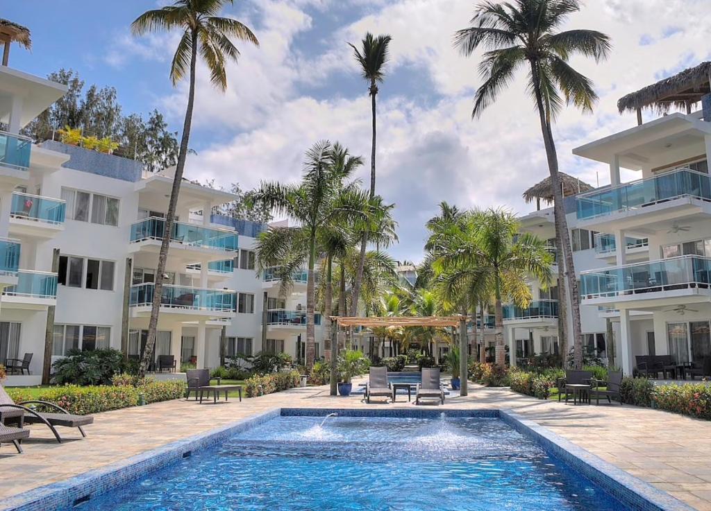 a swimming pool in front of a building with palm trees at Palmeraie Terrenas Beach Apartment in Las Terrenas