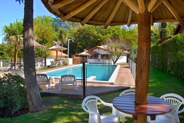 a table and chairs under a wooden umbrella near a pool at Cabañas Los Duendes in Villa General Belgrano