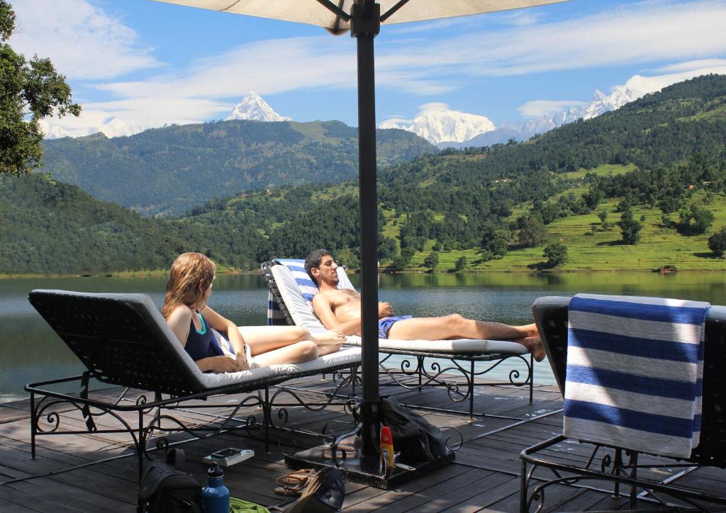 two people sitting in chairs on a deck with a view of a lake at The Begnas Lake Resort & Villas in Pokhara