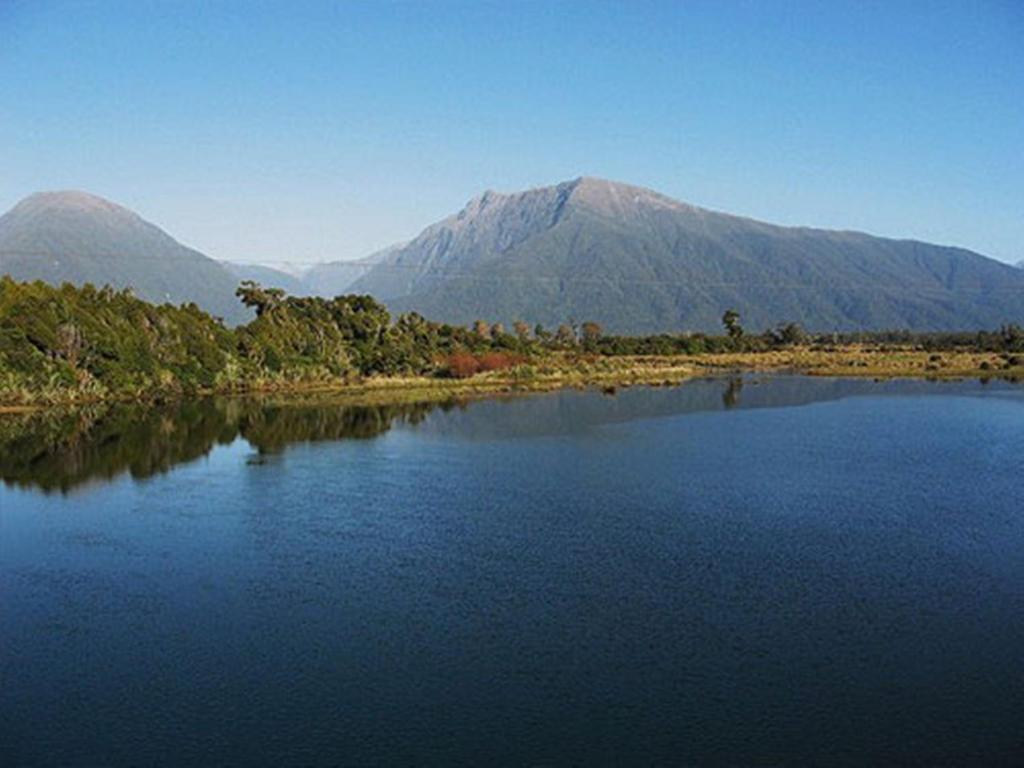 a lake with mountains and a mountain range at Bay Road Motels in Haast