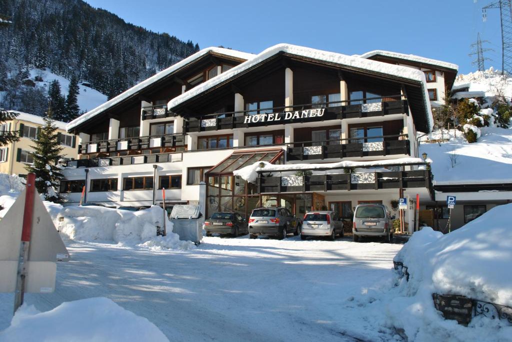 Hotel Daneu Gaschurn في غاسشرن: مبنى الفندق مع وجود سيارات تقف في الثلج