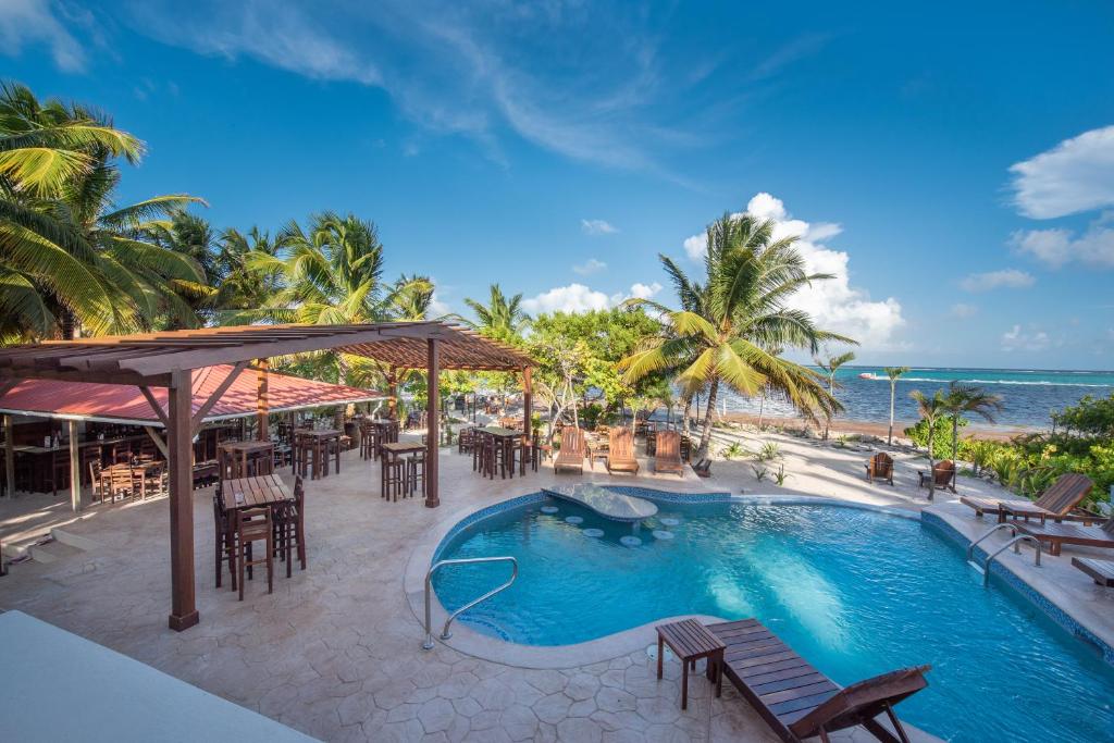 una piscina con mesas y sillas y el océano en Bella Vista Resort Belize en San Pedro