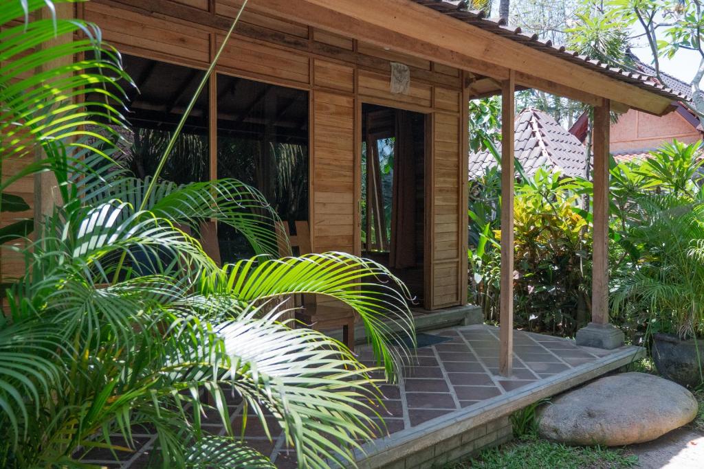 a wooden house with a porch in a garden at Segara Urip in Negara