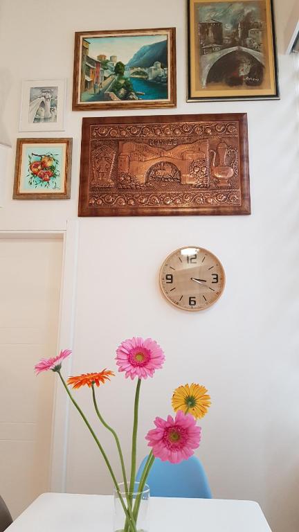 eine Vase mit Blumen und eine Uhr an der Wand in der Unterkunft Galeria Nura in Mostar