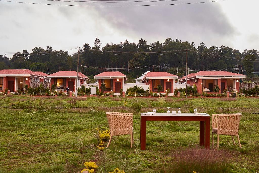 two chairs and a table in a field with houses at Sixth Element in Kushālnagar