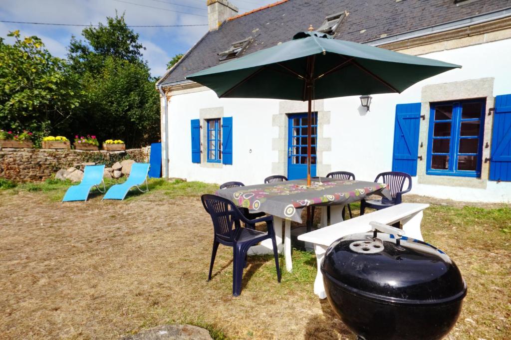 a table with an umbrella next to a grill at La Maison aux Volets Bleus de Prat An Ilis à 900m de la plage du Guilvinec in Le Guilvinec