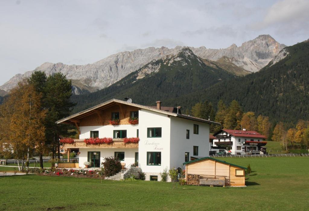 ein weißes Haus auf einem Feld mit Bergen im Hintergrund in der Unterkunft Landhaus Loipe in Leutasch