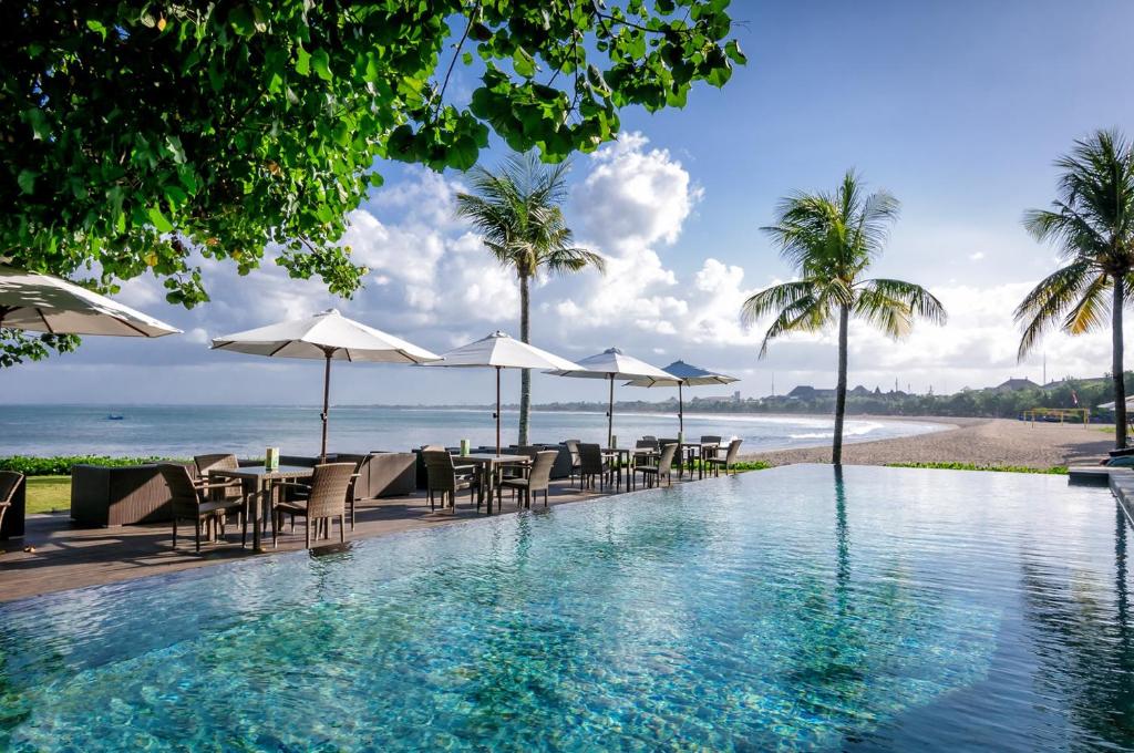 een zwembad met tafels en parasols en het strand bij Bali Garden Beach Resort in Kuta