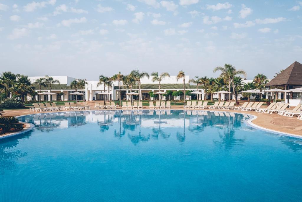 a large blue pool with chairs and palm trees at Iberostar Waves Saidia in Saidia 
