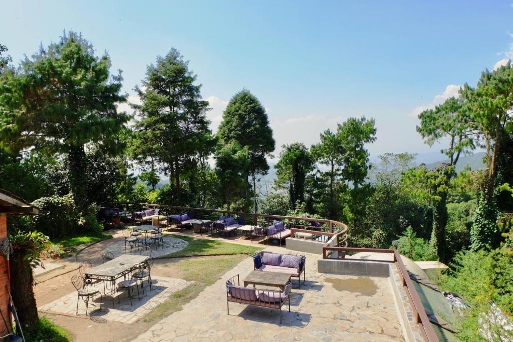 a patio with tables and benches and trees at Hotel At The End Of The Universe in Nagarkot