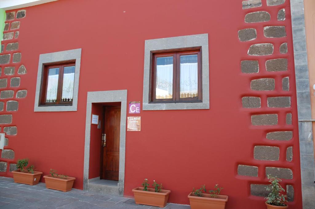 un edificio rojo con tres ventanas y macetas en Casa Rural Carmita, en Vega de San Mateo