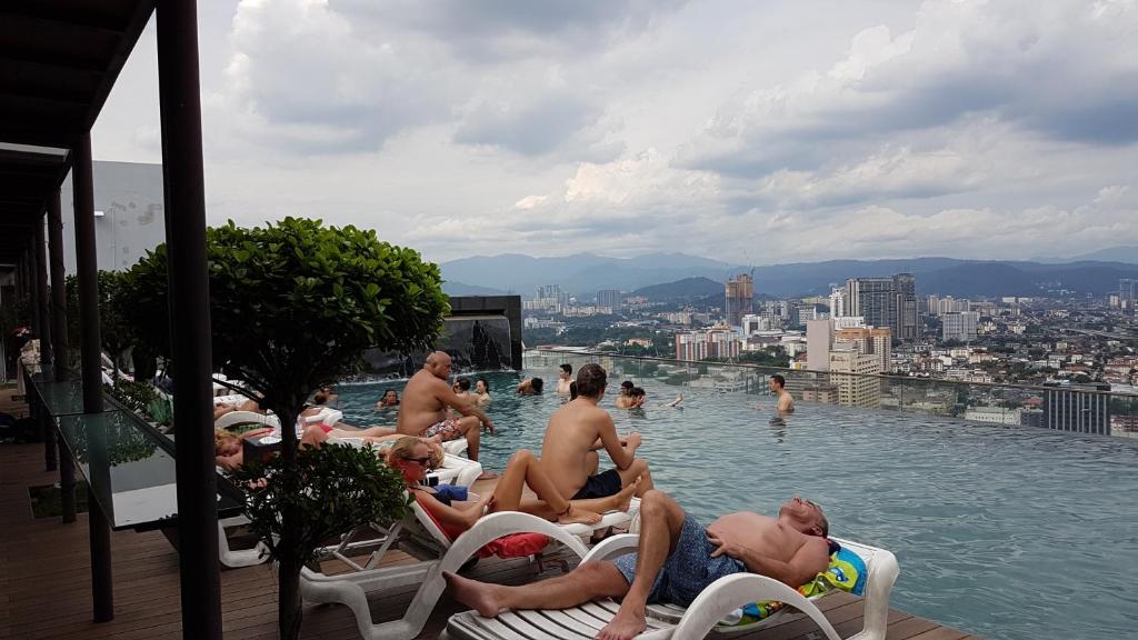 un gruppo di persone seduti su sedie in piscina di SkyBed Over The Sky Hostel @Regalia Suites & Residences KL a Kuala Lumpur