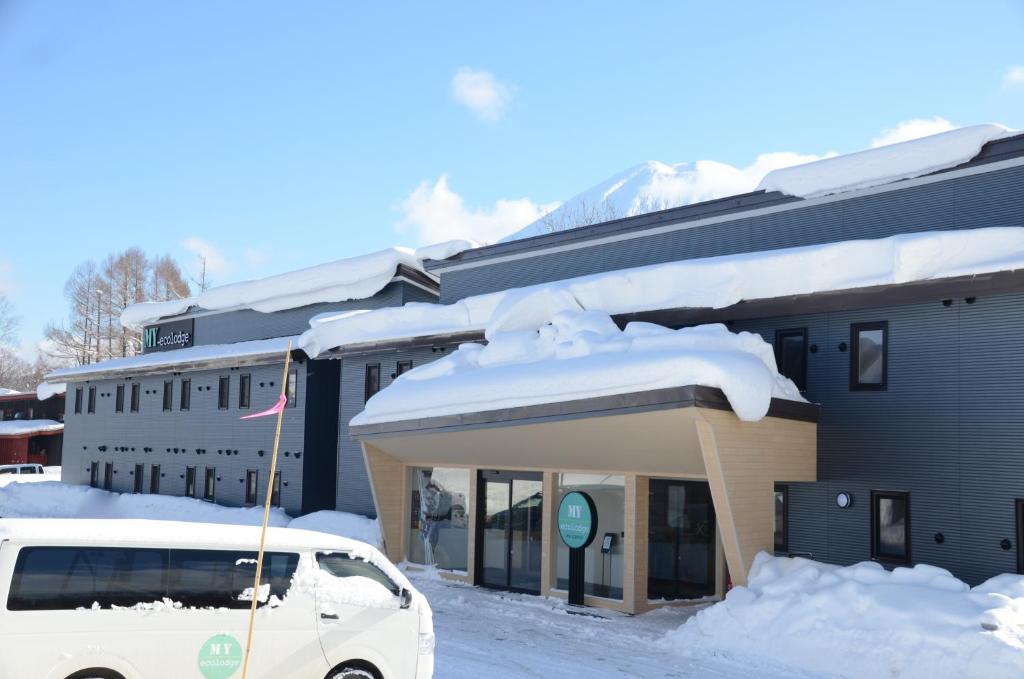 una macchina bianca parcheggiata di fronte a un edificio con neve di My Ecolodge a Niseko