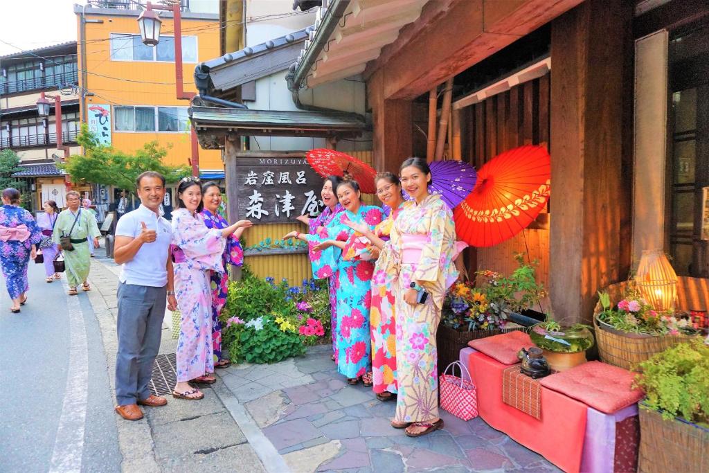 un groupe de personnes debout à l'extérieur d'un immeuble avec parasols dans l'établissement Morizuya, à Toyooka