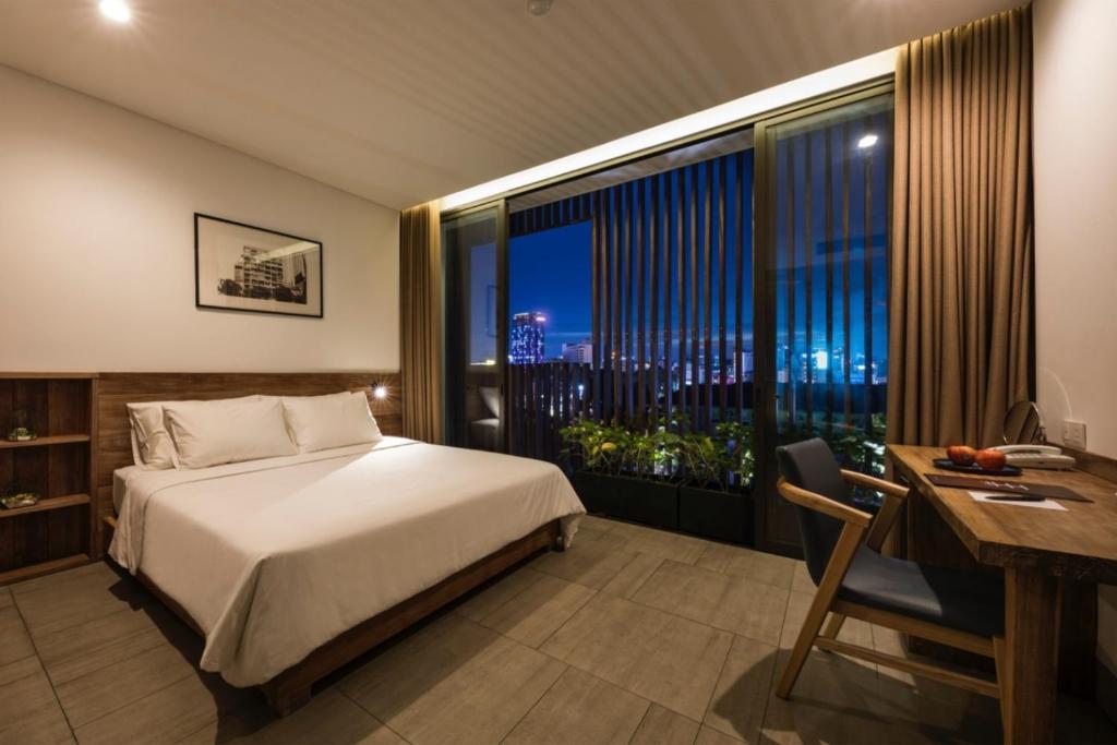 a bedroom with a bed and a desk and a window at Triple E Hotel Fine Art Museum in Ho Chi Minh City