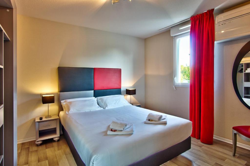 a bedroom with a large bed with red curtains at Adonis Hotel Bayonne in Lahonce