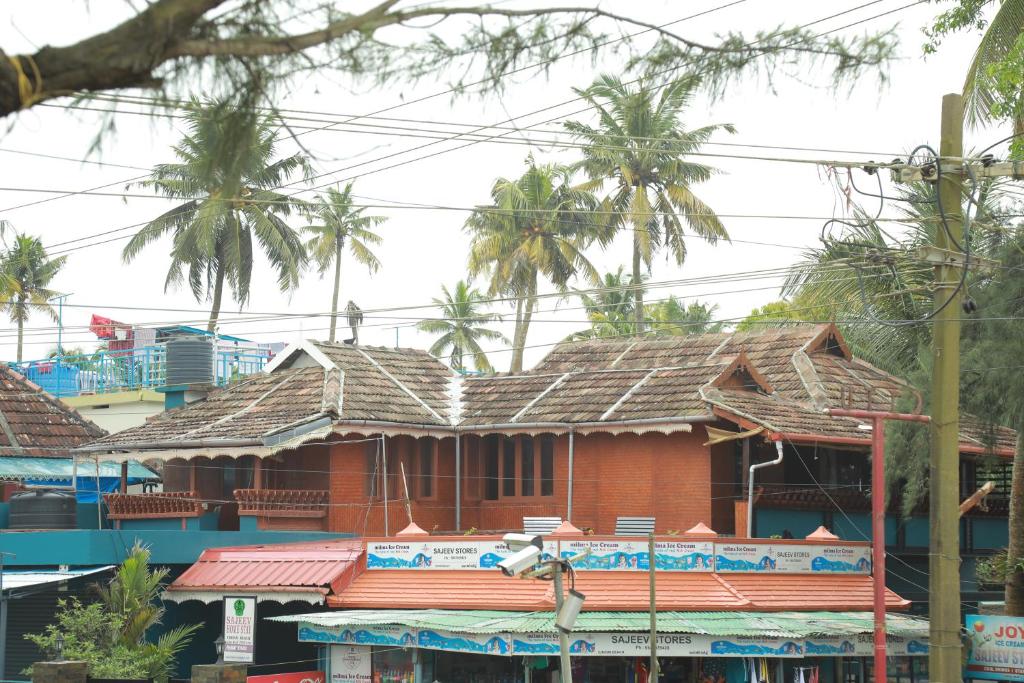 a red house with a shingled roof and palm trees at Sajeev Home Stay in Cherai Beach