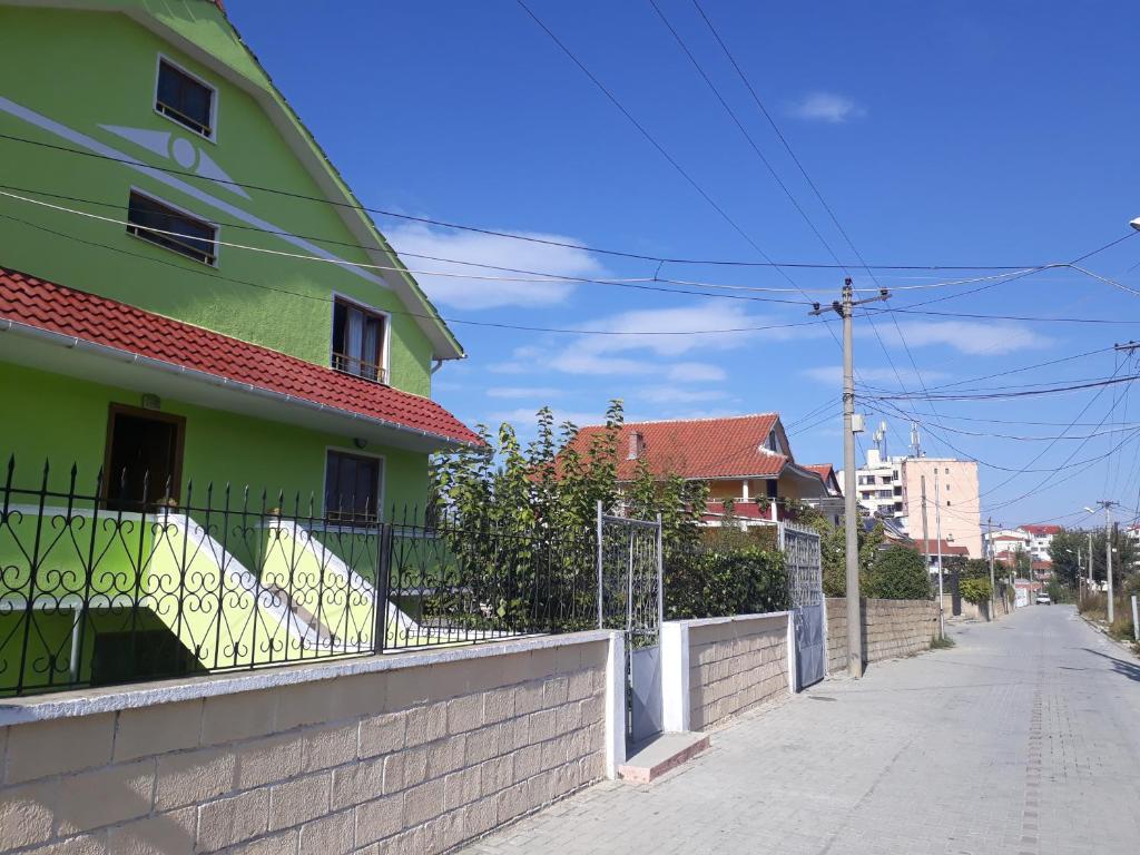 a green building with a fence next to a street at Guest House Pogradeci in Pogradec