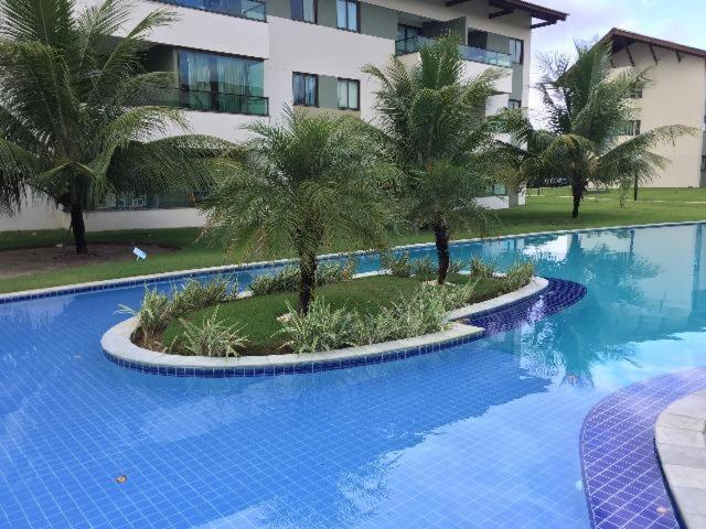 a large swimming pool with palm trees in front of a building at Flat Carneiros Beach Resort in Tamandaré